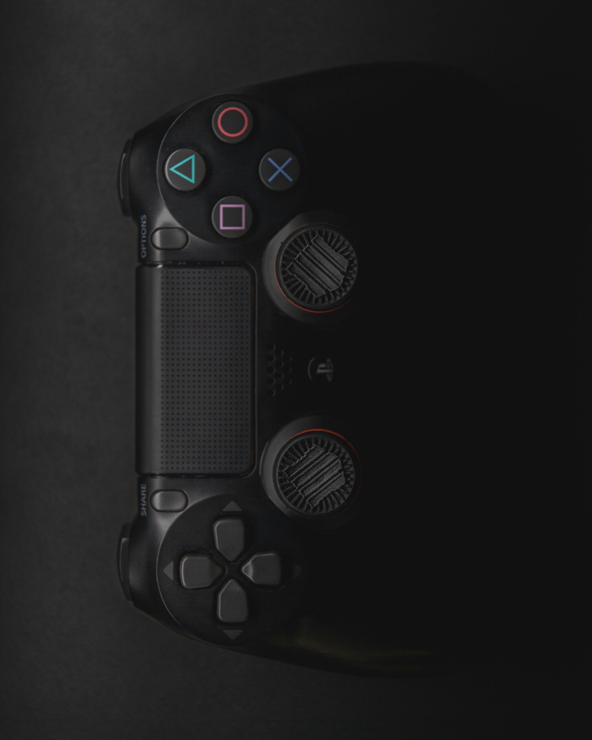 Moody close-up of a black gaming controller in low light with colorful buttons.