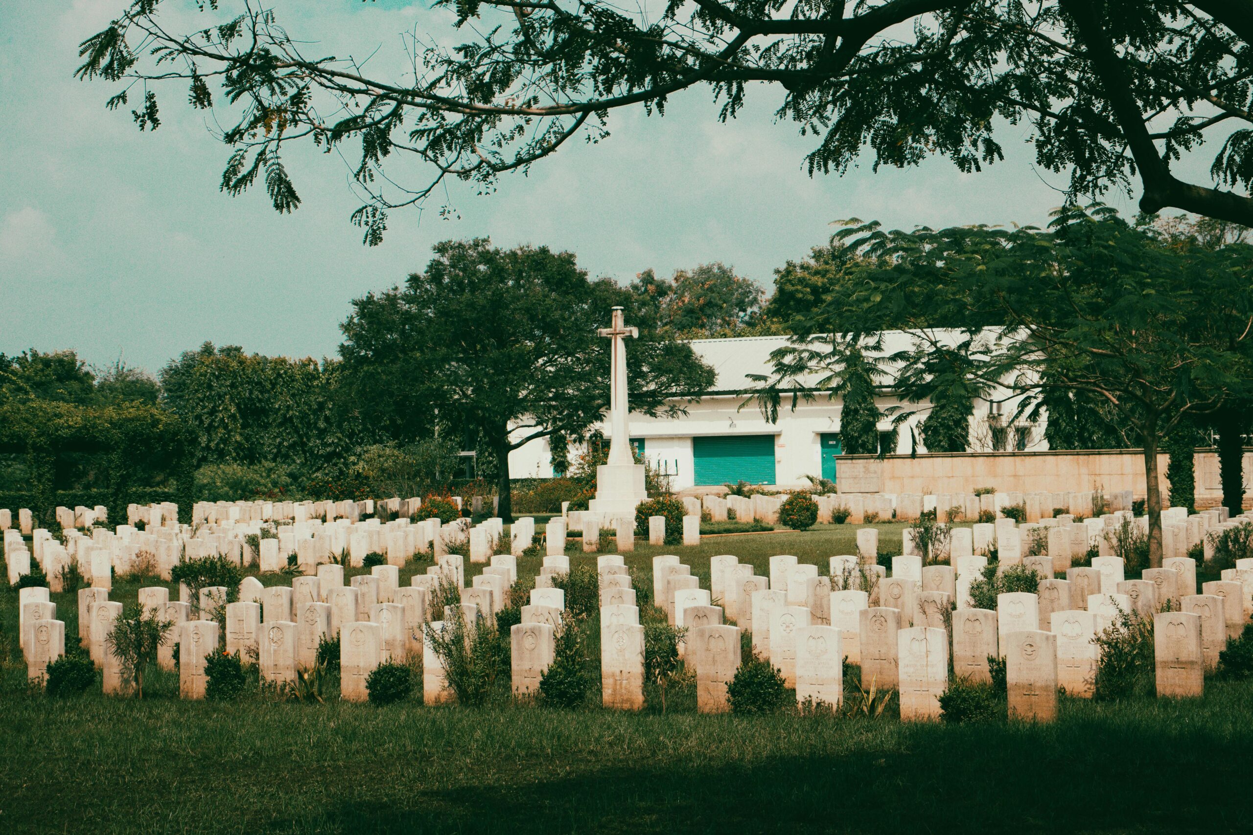 Peaceful view of Madras War Cemetery with rows of tombstones and a central cross amidst lush trees.