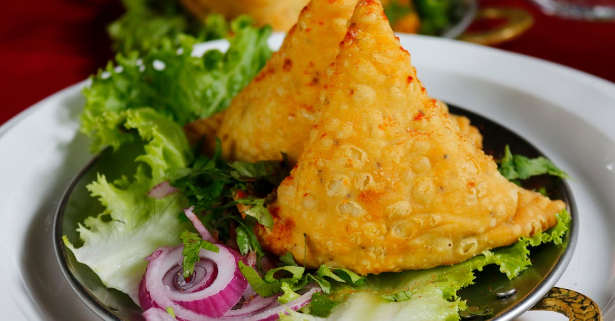 Close-up of crispy samosas served with fresh lettuce and onion rings.