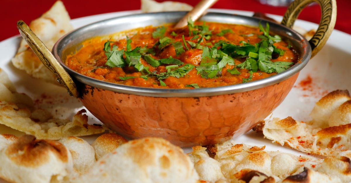 Delicious Indian curry garnished with cilantro served with naan in a copper dish.