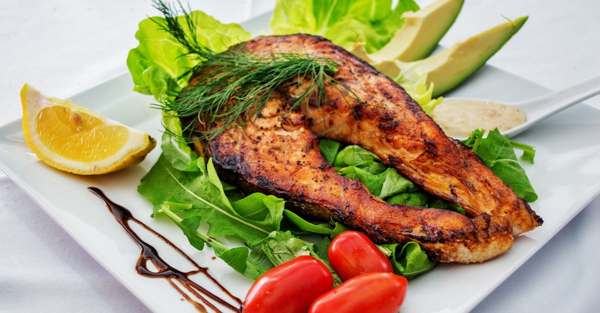 Delicious grilled salmon steak served with avocado, lettuce, cherry tomatoes, and lemon slice on a white plate.