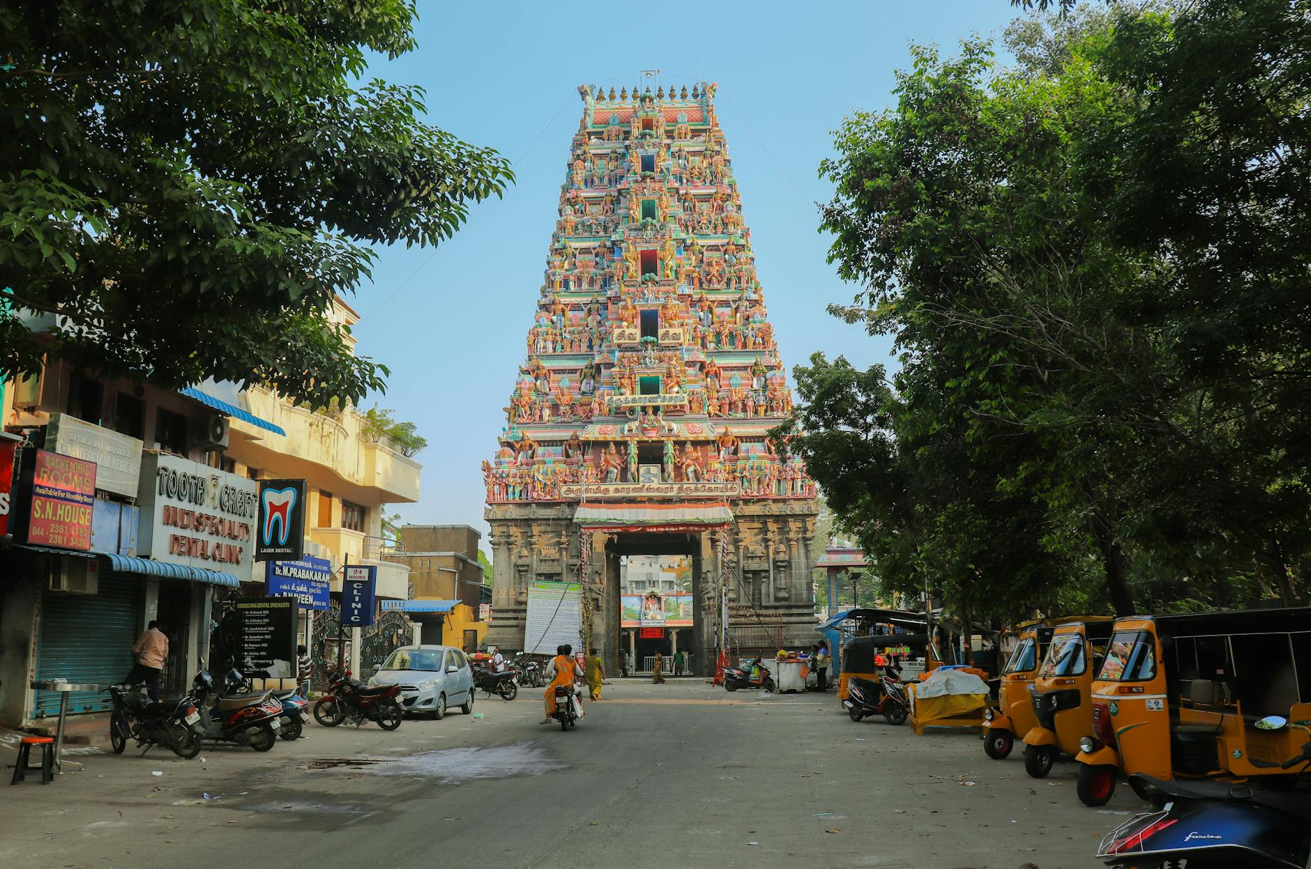 A bustling street view of a colorful Hindu temple in Chennai, India, with auto rickshaws and pedestrians.