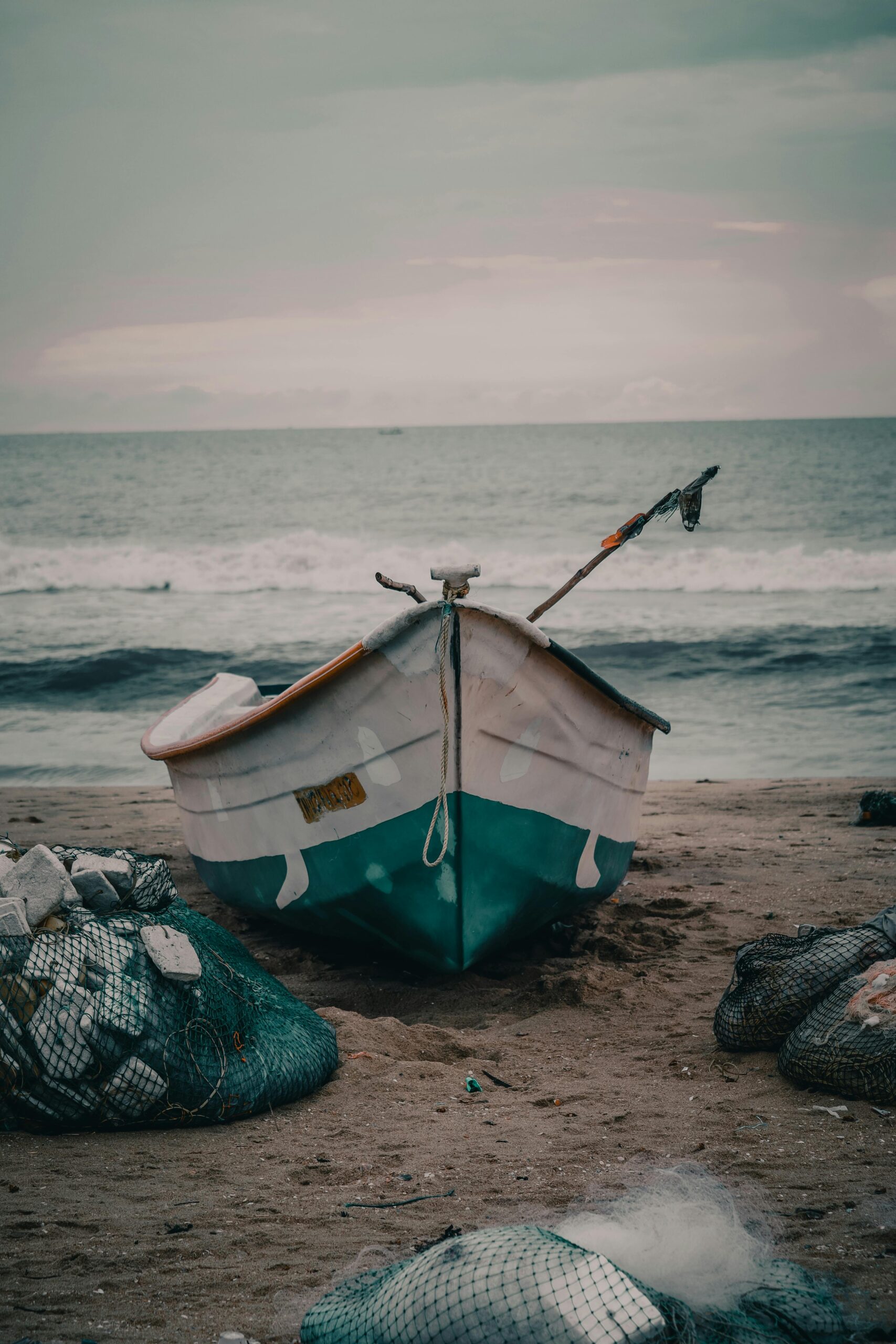 A serene fishing boat rests on the sandy beach of Chennai, India, framed by gentle waves and fishing nets.